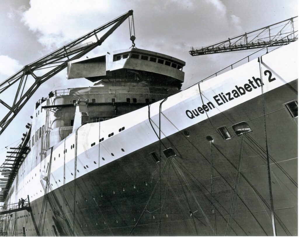The addition of the top deck, wheelhouse and bridge, at the John Brown shipyard, Clydebank, Scotland, in 1968. Photo credit: Cunard Line. From the William H. Miller Collection.