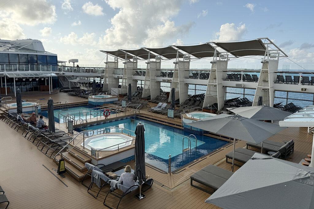 The main pool deck on Celebrity Reflection, with tiered pools, hot tubs, and shaded loungers. Credit: H. Liu