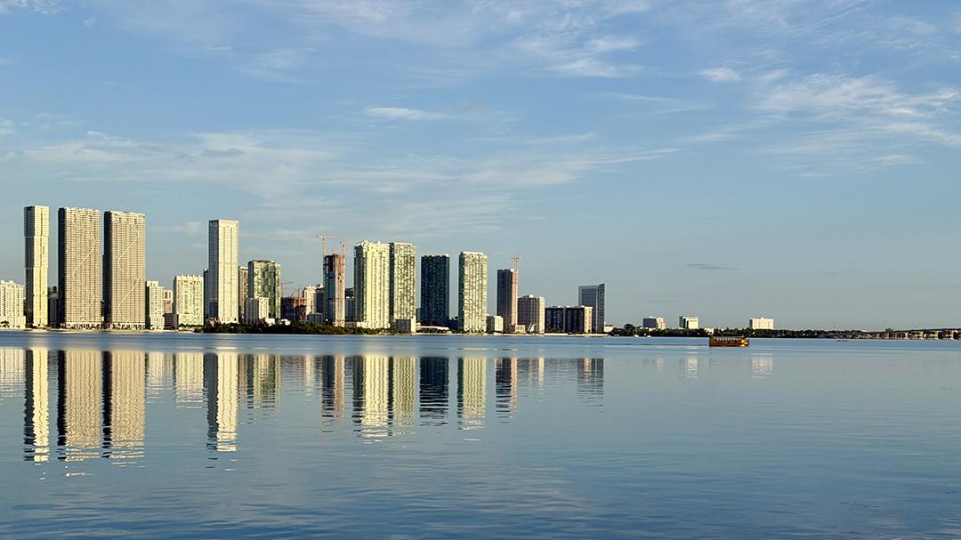 The Miami skyline reflects on calm waters of Biscayne Bay as the Miami Beach Water Taxi makes its morning crossing. Credit: H. Liu