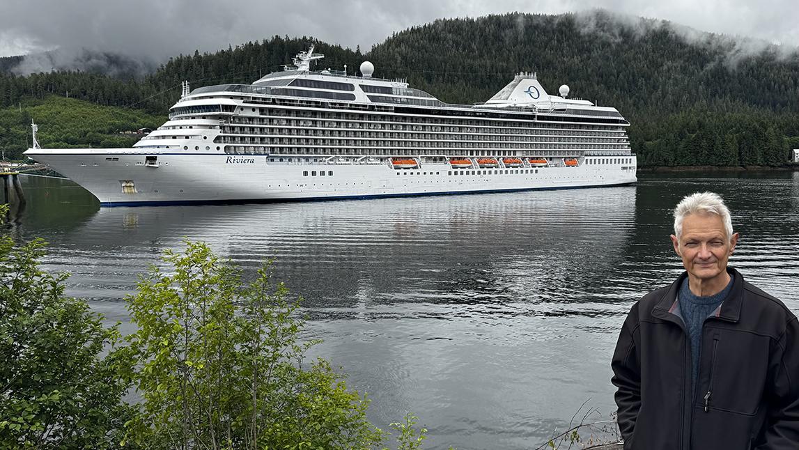 Author Peter Knego poses in front of Oceania Riviera at Ward Cove (Ketchikan), Alaska. Photo by Mike Masino.